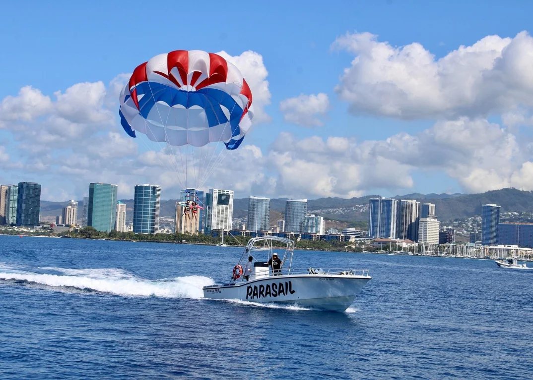 Two flyers in a tandem harness lifting off the back deck of the parasail boat with the canopy filling behind them