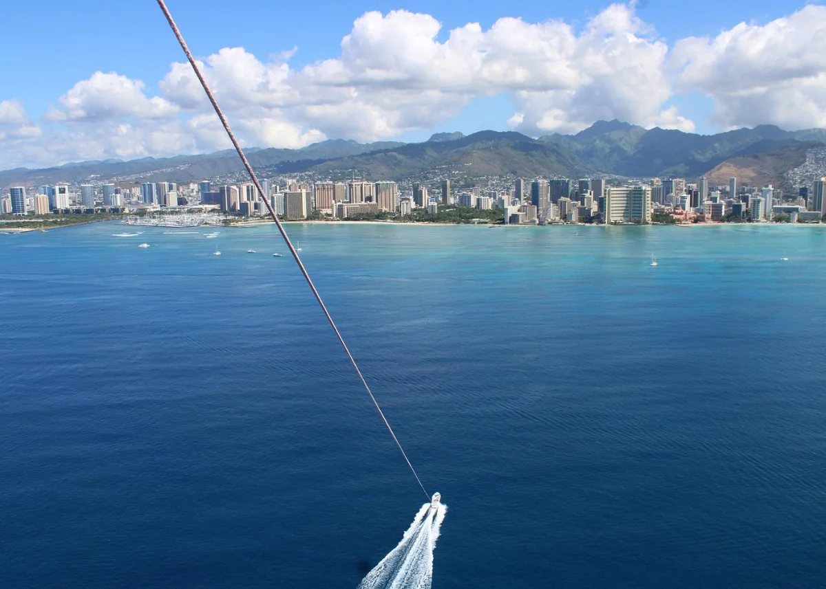 A parasail canopy drifting over Waikiki at golden hour with the hotels along the beach catching the light