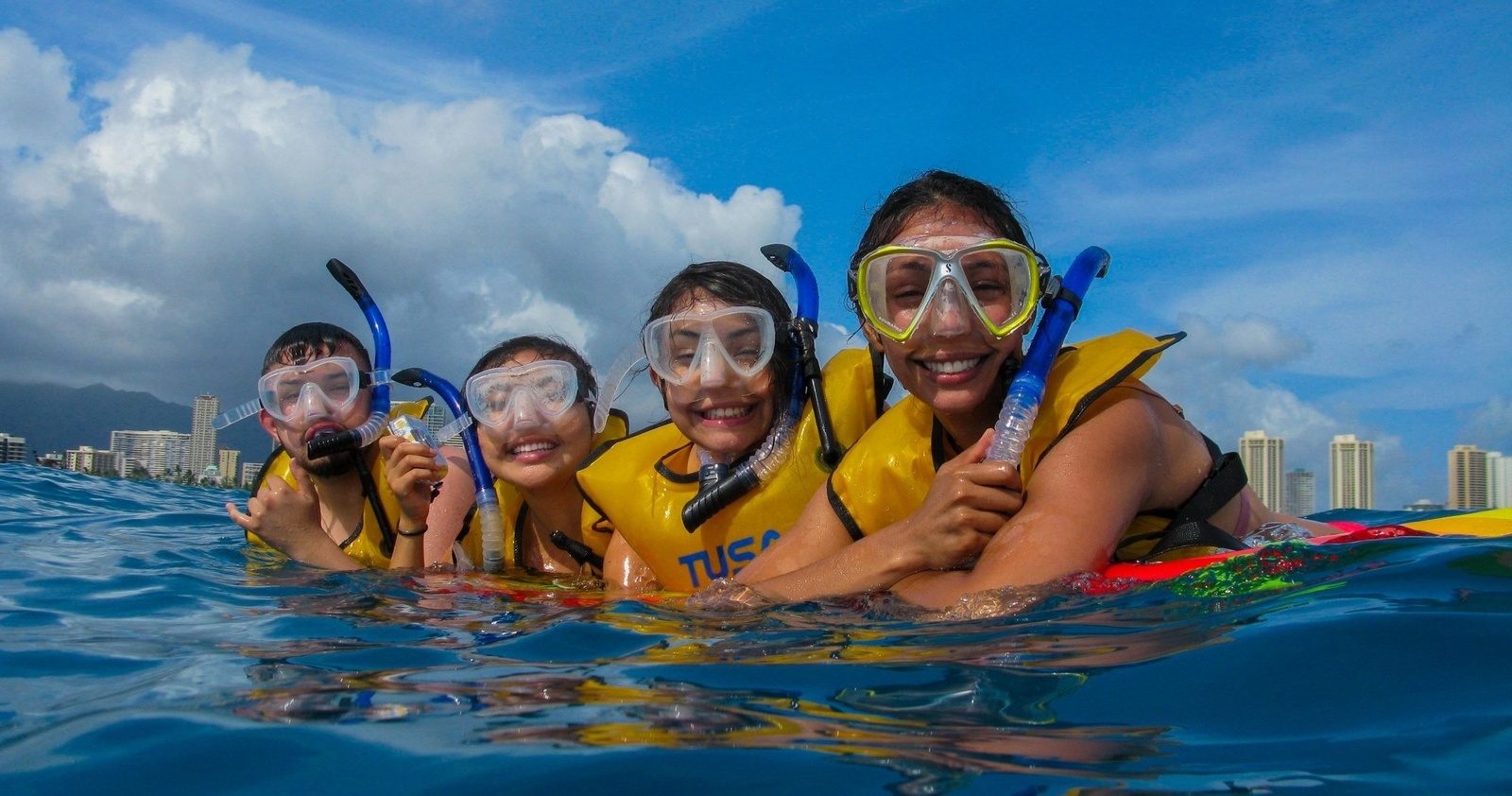 A family in masks and life vests smiling in the water off Waikiki with the hotels behind them